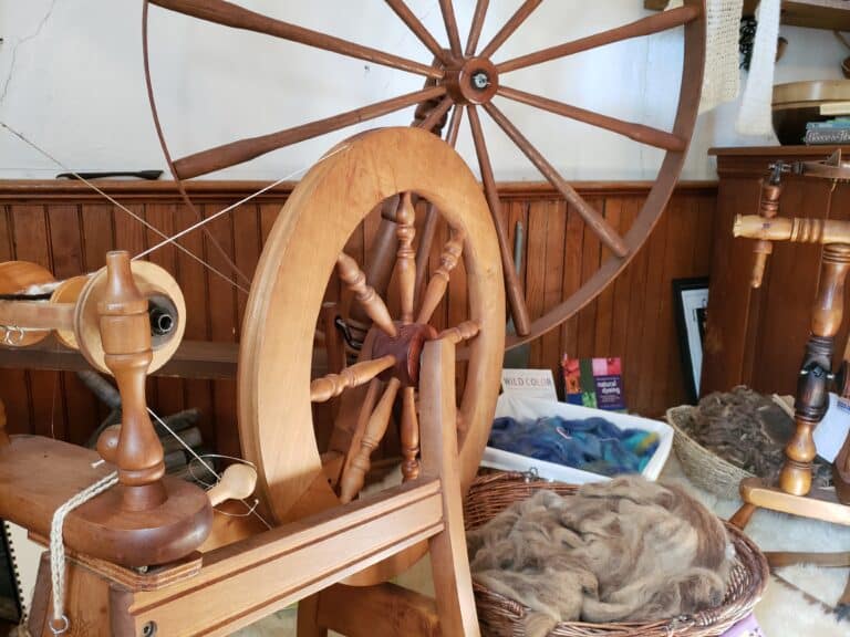 Two wooden spinning wheels displayed in a fiber arts studio alongside wool roving and craft books