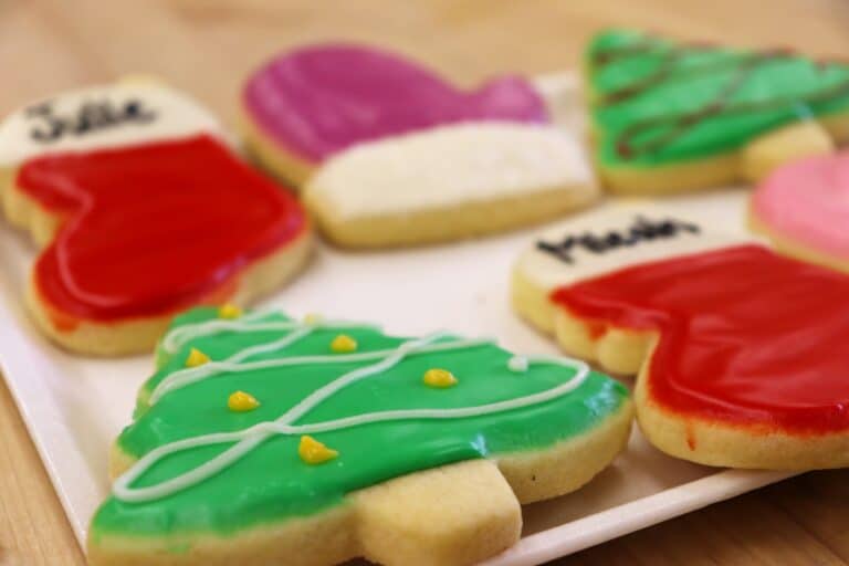 Decorated Christmas sugar cookies shaped like mittens and trees on a white tray