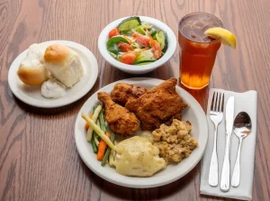 Fried chicken dinner plate with mashed potatoes, vegetables, and stuffing alongside rolls, garden salad, and iced tea at Sauder Village's Barn Restaurant