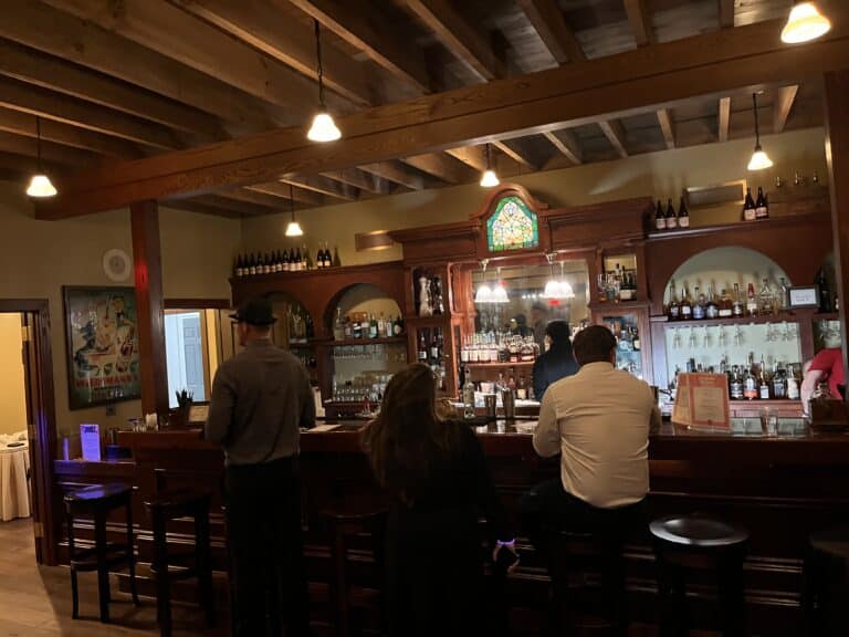 Warm, wood-paneled bar inside Sauder Village's restaurant, guests seated beneath exposed beam ceiling