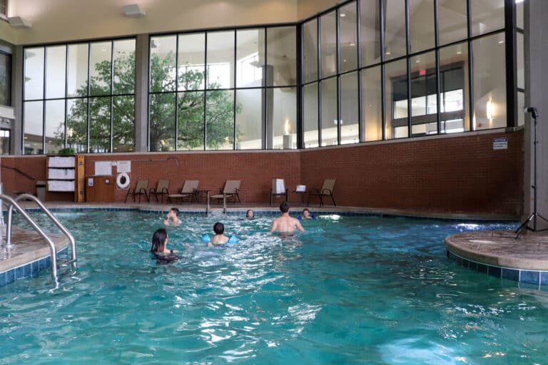 Guests swimming in the indoor pool at Sauder Village's Heritage Inn, with large windows overlooking trees