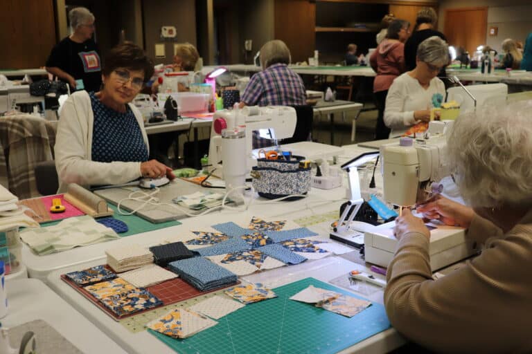 Quilters working at sewing machines during quilting classes at Sauder Village, fabric pieces spread across long tables