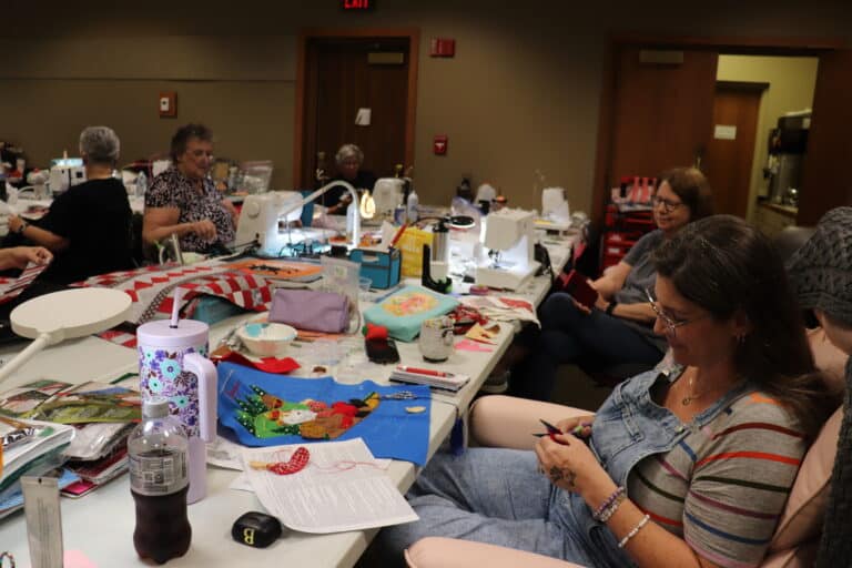 Women hand-stitching and quilting at long tables during a maker retreat at Sauder Village
