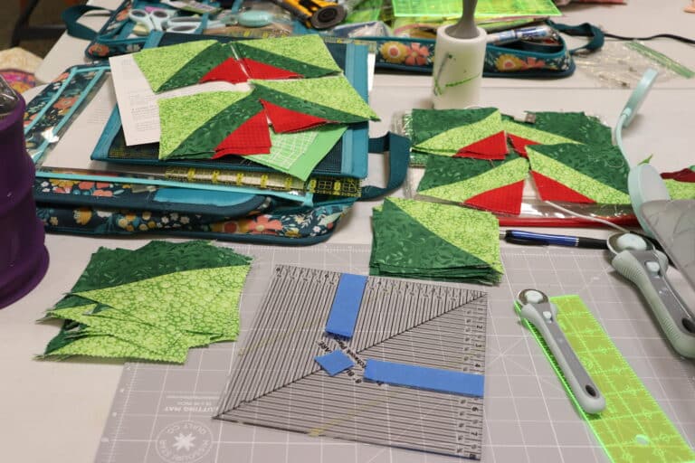Green and red quilt blocks, rotary cutter, and cutting mat on a worktable at a maker retreat