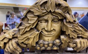 Detailed wood carving of a smiling green man face framed by oak leaves and acorns at a craft show
