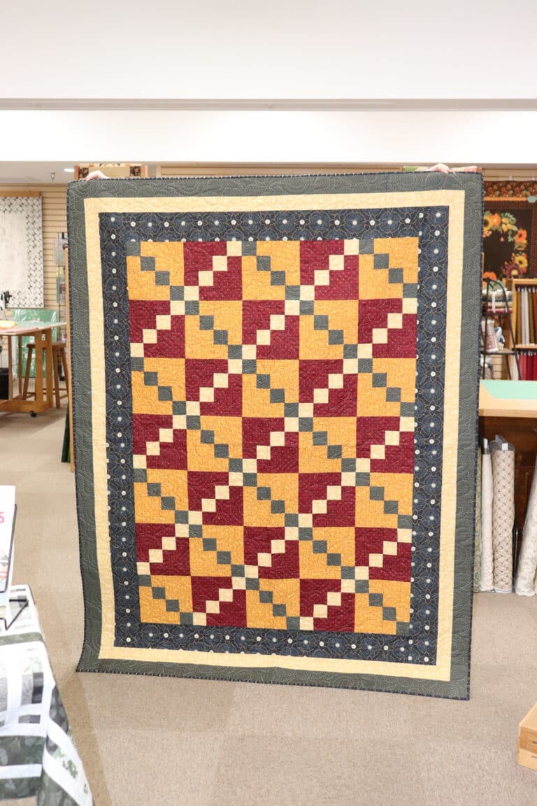 Handmade quilt in gold, burgundy, and navy displayed at Sauder Village's quilting retreat