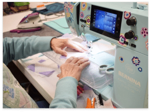 Hands guiding fabric through a Bernina sewing machine during a quilting class