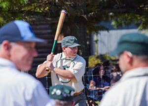 A young ballplayer in vintage uniform winds up to bat during a living-history baseball game