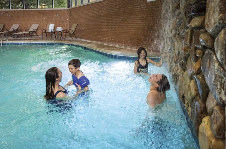 Family splashing together in an indoor pool beneath a stone waterfall feature