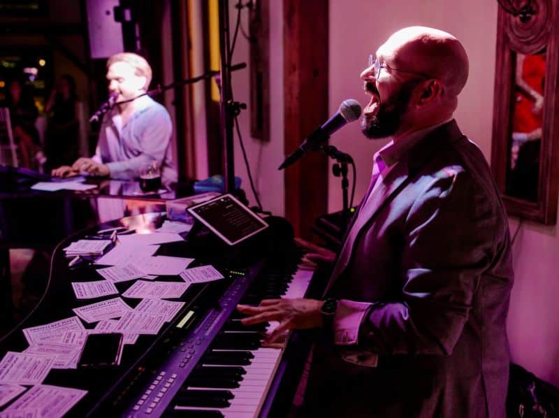 Two pianists performing at Dueling Pianos under purple stage lights