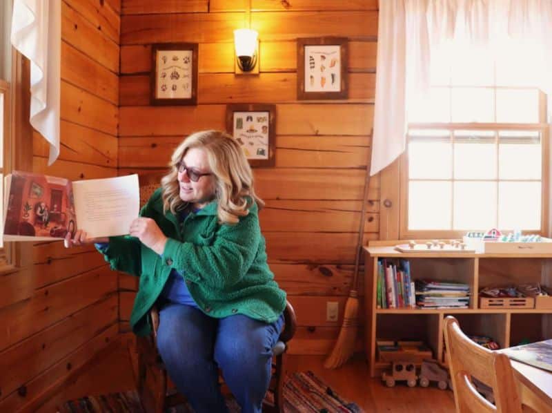 Storyteller reading a picture book inside a historic log home