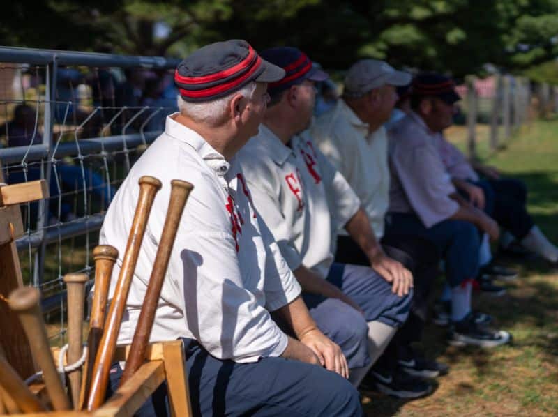 Vintage base ball players in period uniforms seated on a bench with wooden bats