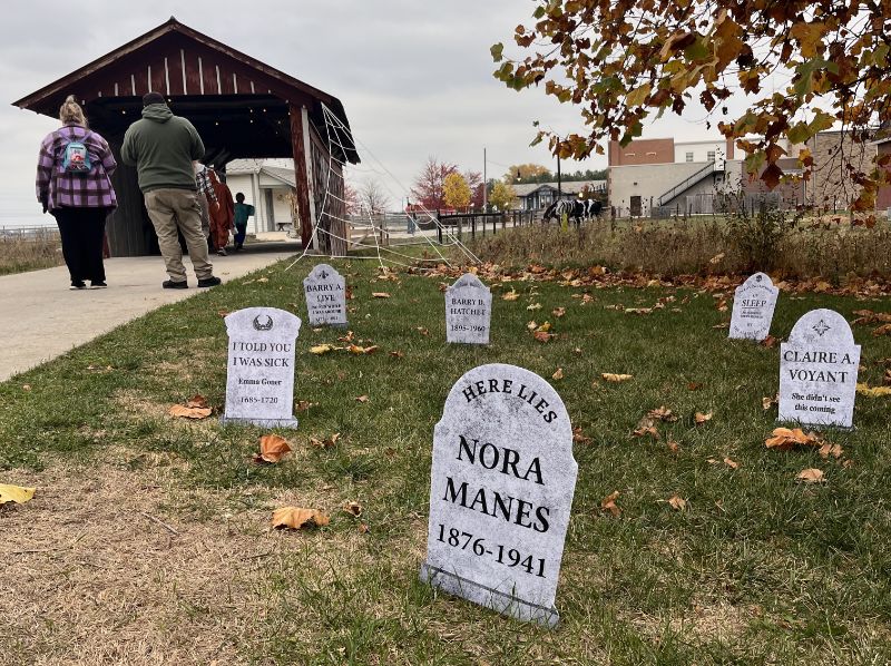 Visitors walking past Halloween tombstone decorations near a covered bridge
